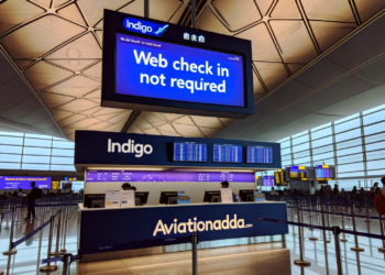 Photo of an IndiGo airline counter inside an airport terminal. Above the counter, a digital signboard displays in bold, clear letters_ 'Web Check in not required